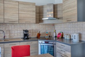 Eine moderne Küche mit Holzschränken, einer Edelstahl-Dunstabzugshaube, einer Kaffeemaschine und einem Wasserkocher auf der Arbeitsfläche.