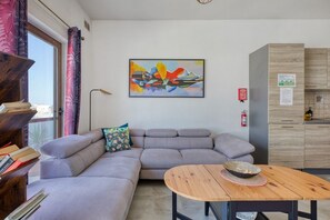 A modern living room with a grey sectional sofa, a wooden coffee table, and a colorful abstract painting on the wall. - the Queen Freddy Penthouse (Ta` Xbiex)