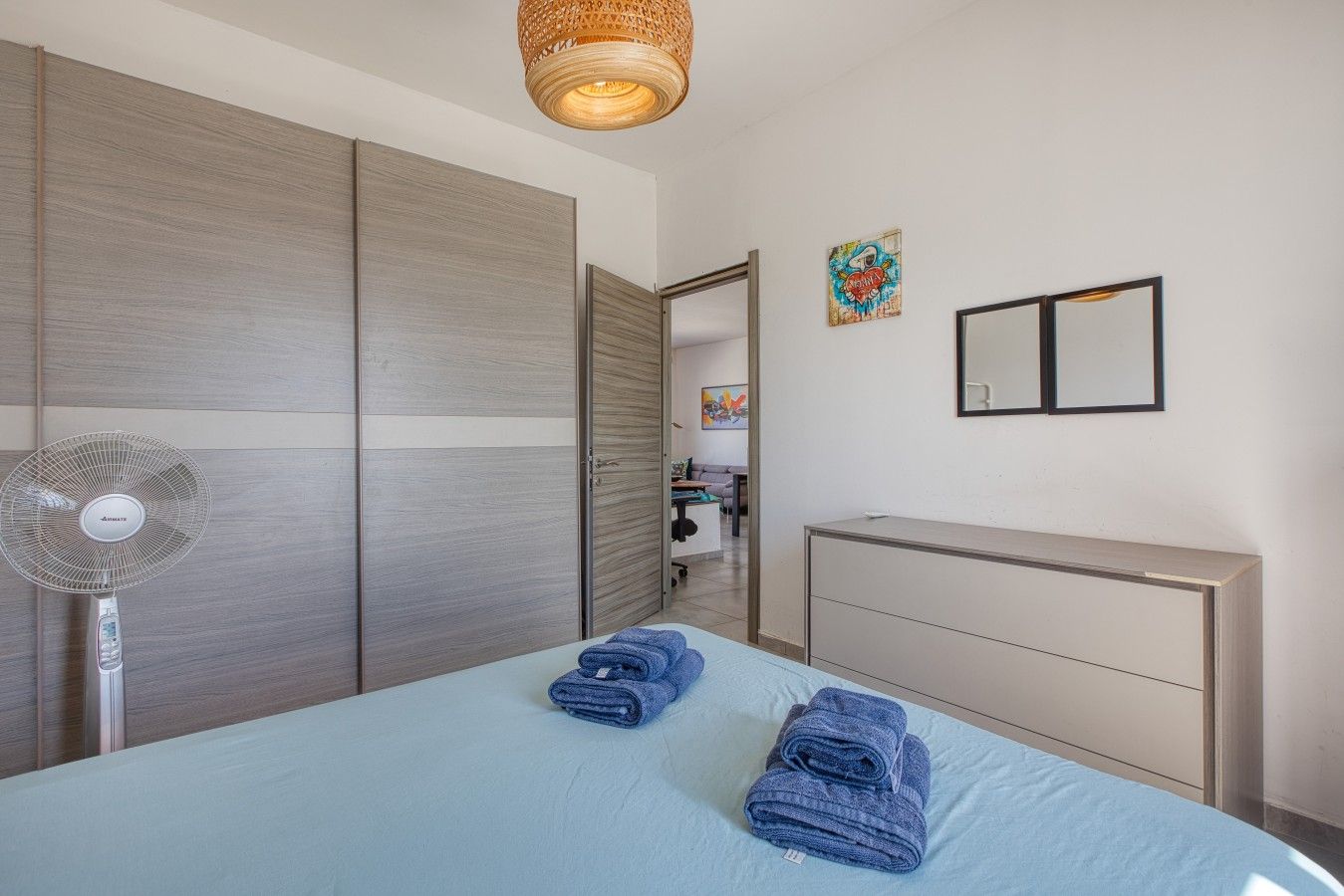 A bedroom with a bed, a bedside fan, a dresser, and a wardrobe.