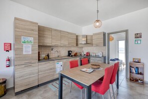 A modern kitchen with wooden cabinets, a dining table with red chairs, and a visible fire extinguisher. - the Queen Freddy Penthouse (Ta` Xbiex)