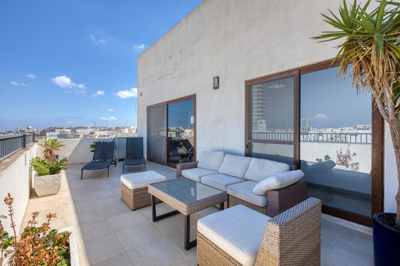 A rooftop terrace with a sofa set, a table, and potted plants.