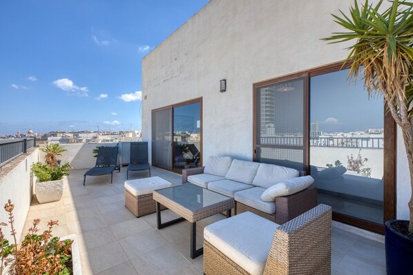 A rooftop terrace with a sofa set, a table, and potted plants.
