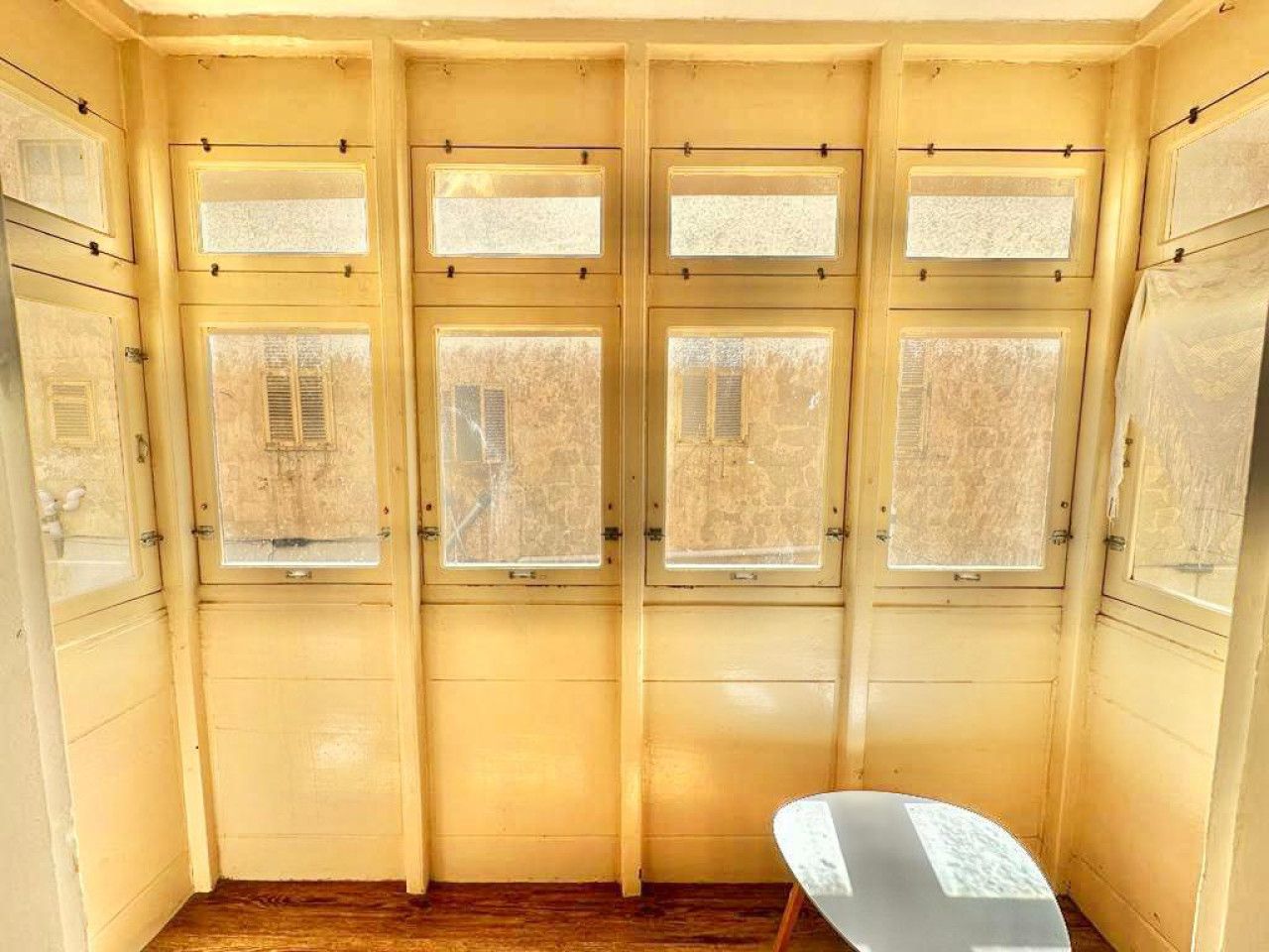 Una habitación con cuatro ventanas, una silla blanca y suelo de madera.