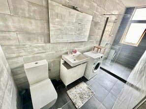 Une salle de bain moderne équipée de toilettes, d’un lavabo et d’un lave-linge, avec un mur en pierre et un puits de lumière.
