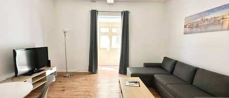 A modern living room with a flat-screen TV, a sofa, a coffee table, and a desk.