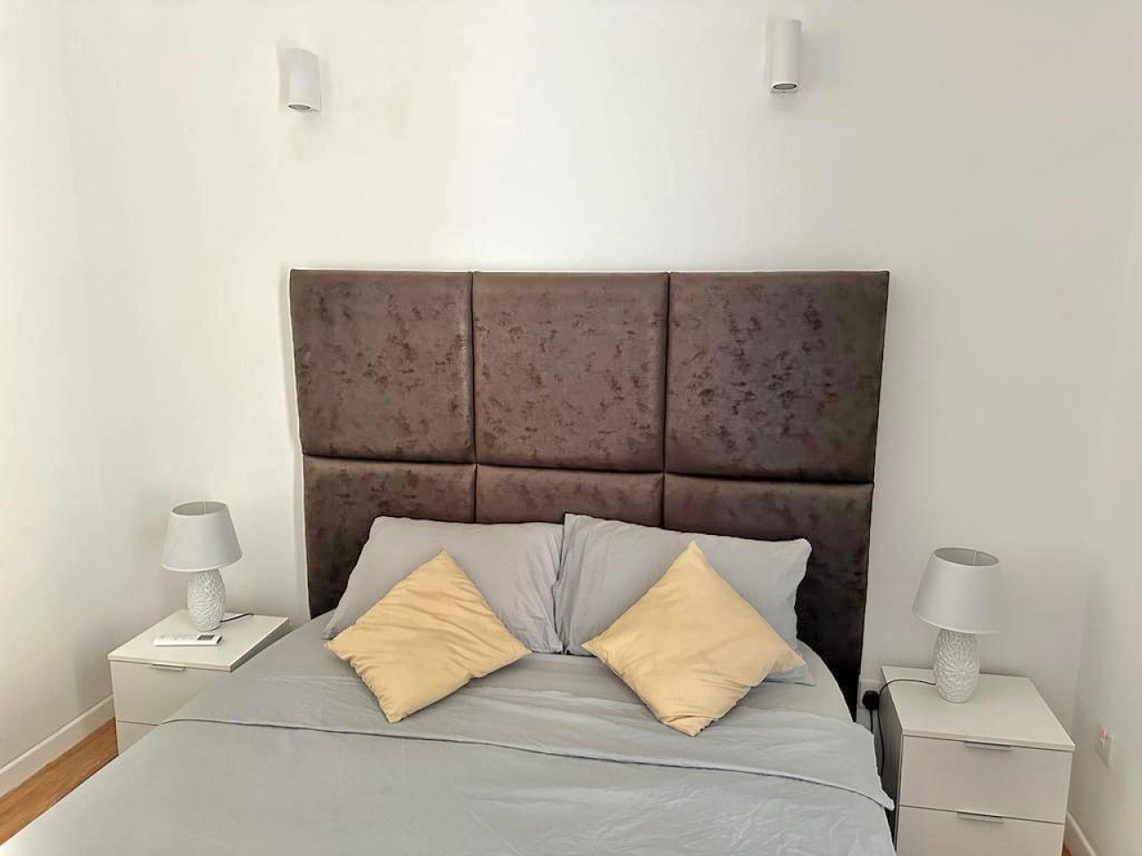 A bed with a padded headboard, two bedside tables with lamps, and a grey bedspread.
