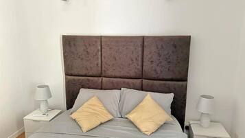 A bed with a padded headboard, two bedside tables with lamps, and a grey bedspread.