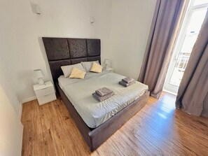 Un lit bien fait, avec une tête de lit, deux tables de chevet et une fenêtre avec des rideaux.