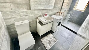 Ein modernes Badezimmer mit Toilette, Waschbecken und Waschmaschine, mit einer Steinwand und einem Oberlicht.