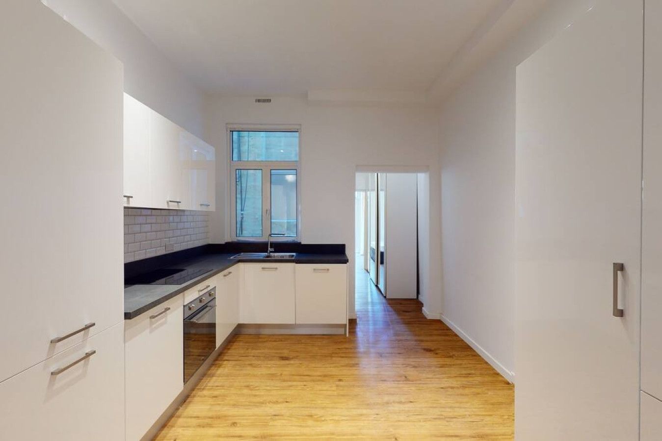 A narrow kitchen with white cabinets, a black countertop, and a wooden floor.