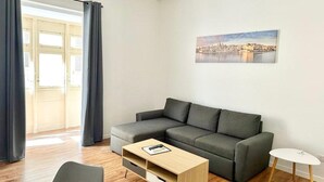 Una sala de estar moderna con un sofá gris, una mesa de centro de madera y una mesita auxiliar blanca.