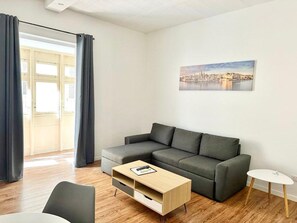 Un salon moderne avec un canapé gris, une table basse en bois et une petite table d’appoint blanche.