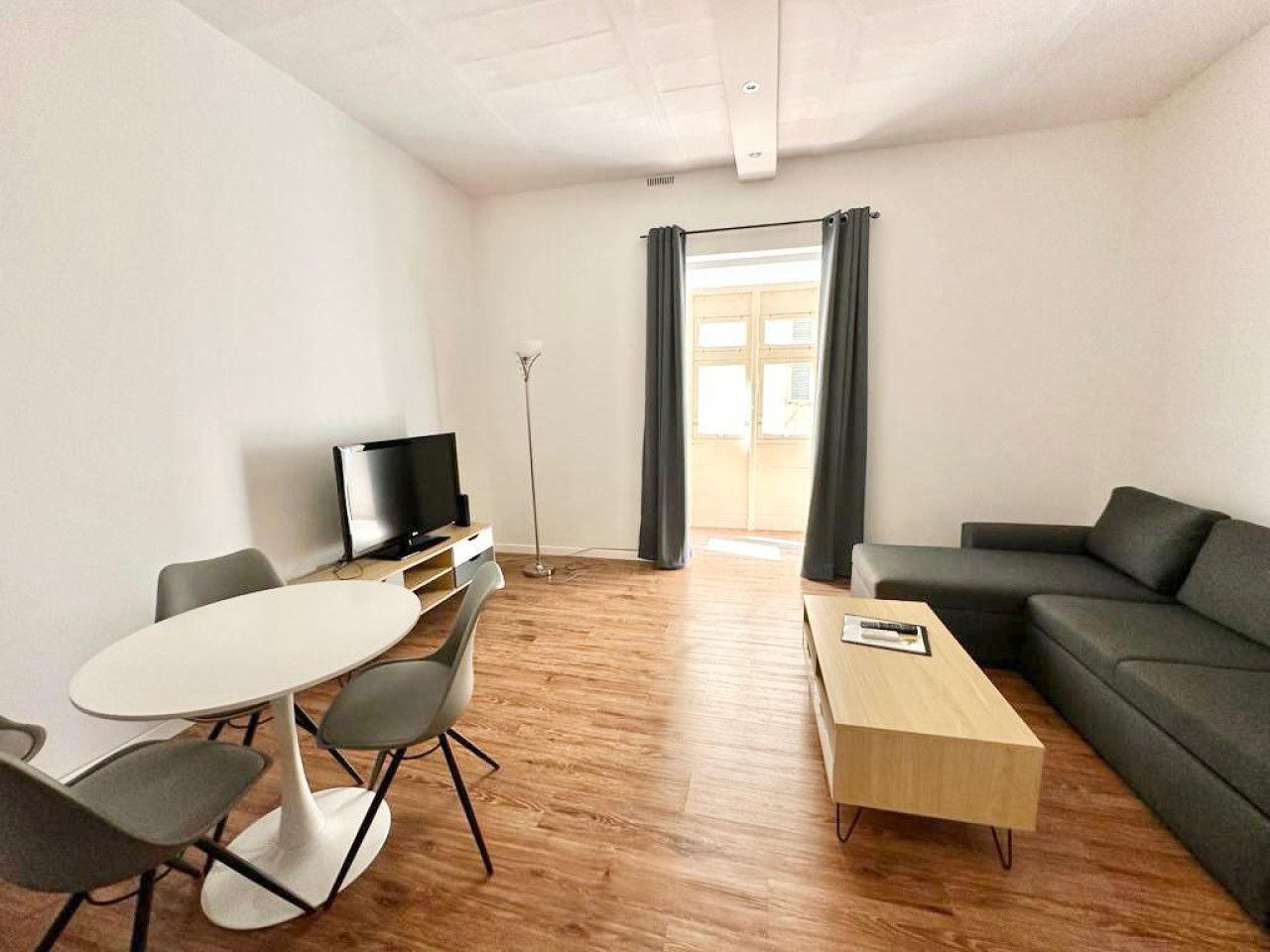 Una sala moderna con sofá, una mesa de centro, televisor y un área de comedor con sillas y una mesa.