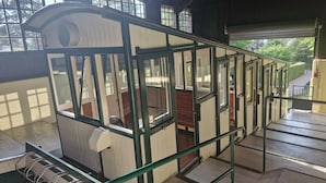 A train station platform with a green metal railing, a wooden bench, and a white building with windows. - Chalet Panoramique Avec Sauna Avec vue sur le LAC Leman et Montagnes (Évian-les-Bains)