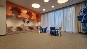 Un hall d’hôtel moderne doté d’un espace salon, d’une carte du monde accrochée au mur et de grandes fenêtres ornées de rideaux légers.