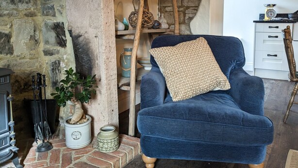 A cozy living room with a blue armchair, a stone fireplace, and a rustic ladder shelf.