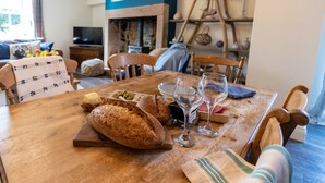 A wooden dining table with bread, wine glasses, and a candle. There is a fireplace, a blue wall with framed pictures, and a wooden ladder against the wall.