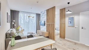 A modern hotel room with a dining area, a sofa, a TV, and a wooden partition. - Apartamenty Świnoujście - Seaside Garden (Swinoujscie)
