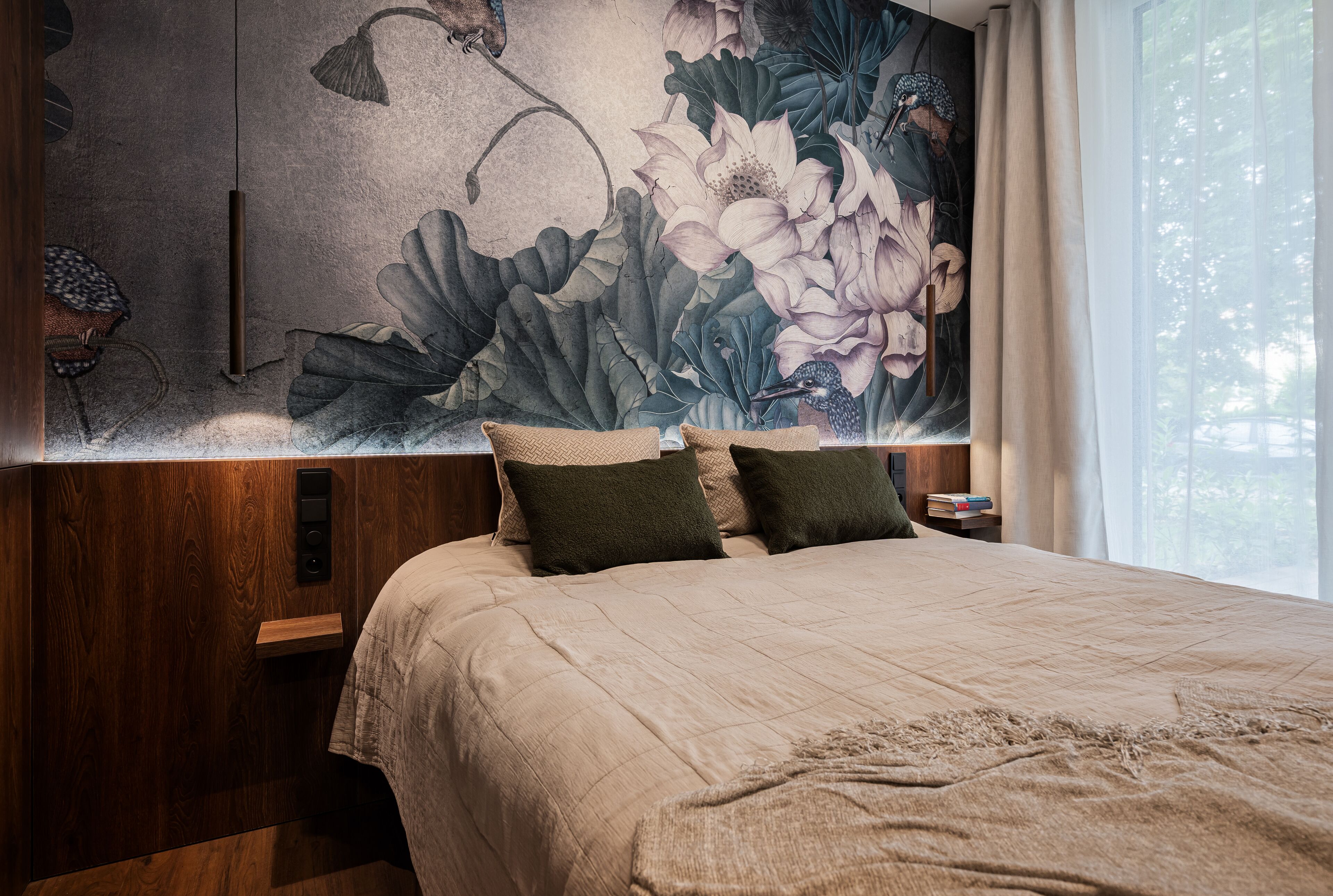 A bedroom with a large floral mural on the wall, a wooden headboard, and a bedside table with books.