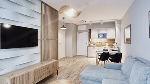 A modern living room with a flat-screen TV, a wooden entertainment unit, and a grey sofa. - Apartamenty Świnoujście - Seaside Garden (Swinoujscie)