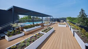 A modern outdoor deck with a pool, wooden walkways, and planters with small trees. - Apartamenty Świnoujście - Seaside Garden (Swinoujscie)