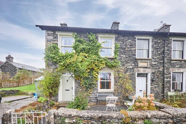 A stone house with a garden, a white door, and a bench.