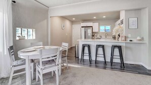 A modern kitchen with white cabinetry, a stainless steel refrigerator, and a bar area with stools. - Mountain view | Games, Patio and BBQ in CO Springs (Colorado Springs)