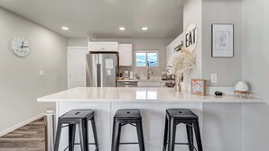A modern kitchen with a large island, white cabinetry, and black bar stools. - Mountain view | Games, Patio and BBQ in CO Springs (Colorado Springs)