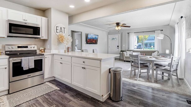 A modern kitchen with white cabinetry, a built-in oven, and a microwave. There is a dining area with a table and chairs, and a ceiling fan above. - Mountain view | Games, Patio and BBQ in CO Springs (Colorado Springs)