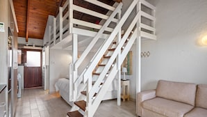 Un vaste espace de vie agrémenté d’un escalier blanc menant à une mezzanine, d’un canapé beige et d’un plafond en bois.