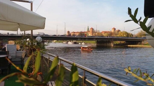 A riverside view with a bridge, boats, and buildings in the background. - The Boat - Hostel&Chill (Kraków)