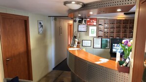 A reception area with a wooden reception desk, a coat rack, a television, and a wall-mounted shoe rack. - The Boat - Hostel&Chill (Kraków)