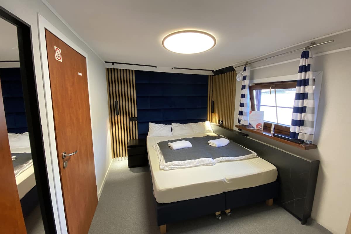 A compact hotel room with a bed, bedside table, and a window with curtains.