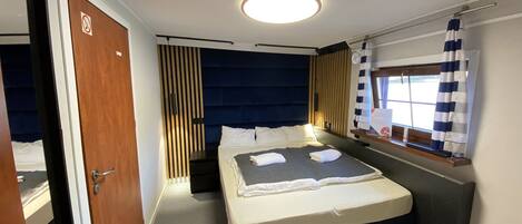 A compact hotel room with a bed, bedside table, and a window with curtains.