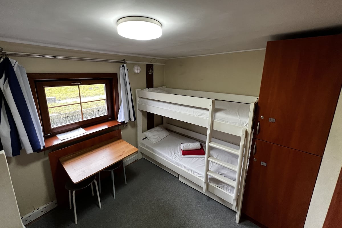 A small, compact room with bunk beds, a desk, and a window.