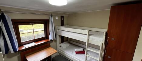 A small, compact room with bunk beds, a desk, and a window.