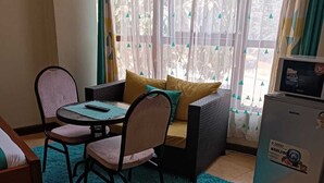 A small, cozy room with a sofa, two chairs, a table, and a refrigerator. - Lux Suites kipande Road Studio Apartment (Nairobi)