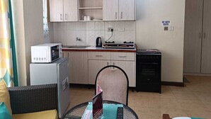 A compact kitchen with white cabinets, a microwave, a stove, and a small refrigerator. - Lux Suites kipande Road Studio Apartment (Nairobi)