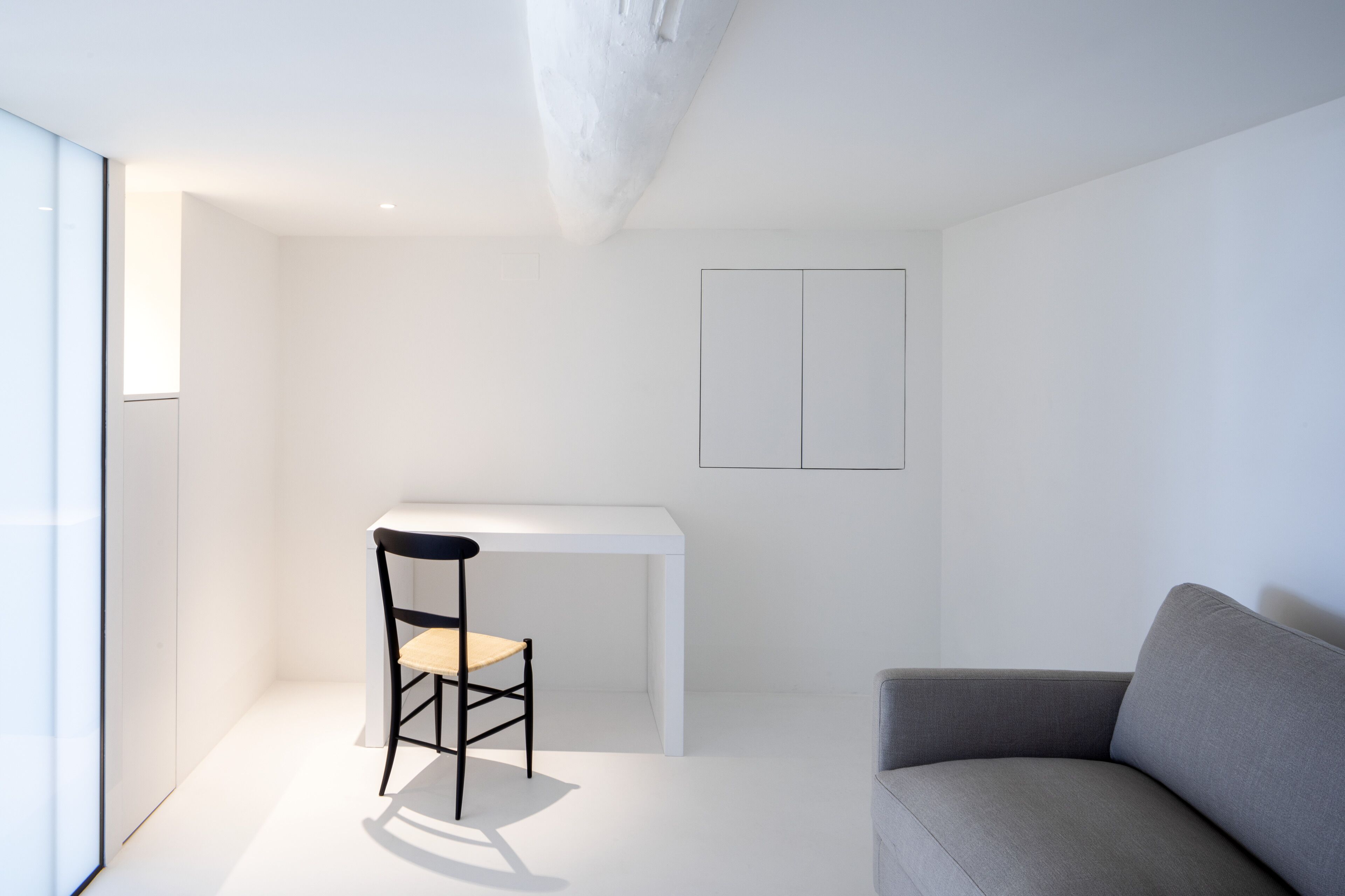 Ein minimalistisches Wohnzimmer mit einem weißen Tisch, einem schwarzen Sessel und einem grauen Sofa.
