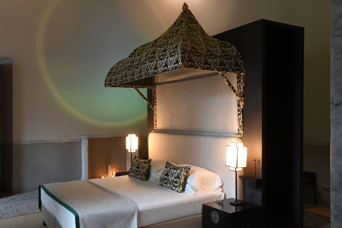 A hotel room with a bed, two bedside lamps, a patterned canopy, and a nightstand.
