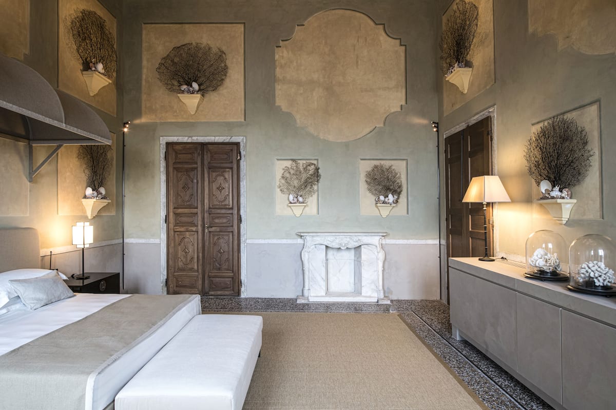 A hotel room with a large bed, a nightstand, a dresser, and a fireplace.
