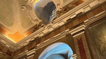 An ornate ceiling with a large mirror and a window.