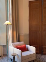 Een kamer met een witte fauteuil, een klein rond tafeltje, een vloerlamp en een houten deur.