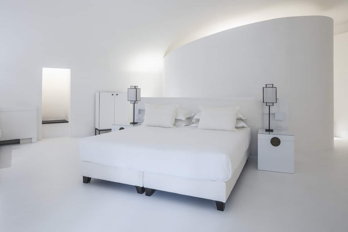 A modern bedroom with a white bed, nightstands, and a curved wall.