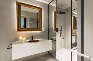 A modern bathroom with a white vanity, a gold-framed mirror, and a glass-enclosed shower.