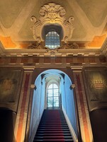 Una imponente escalera con detalles arquitectónicos elaborados, que conduce a un amplio ventanal arqueado.