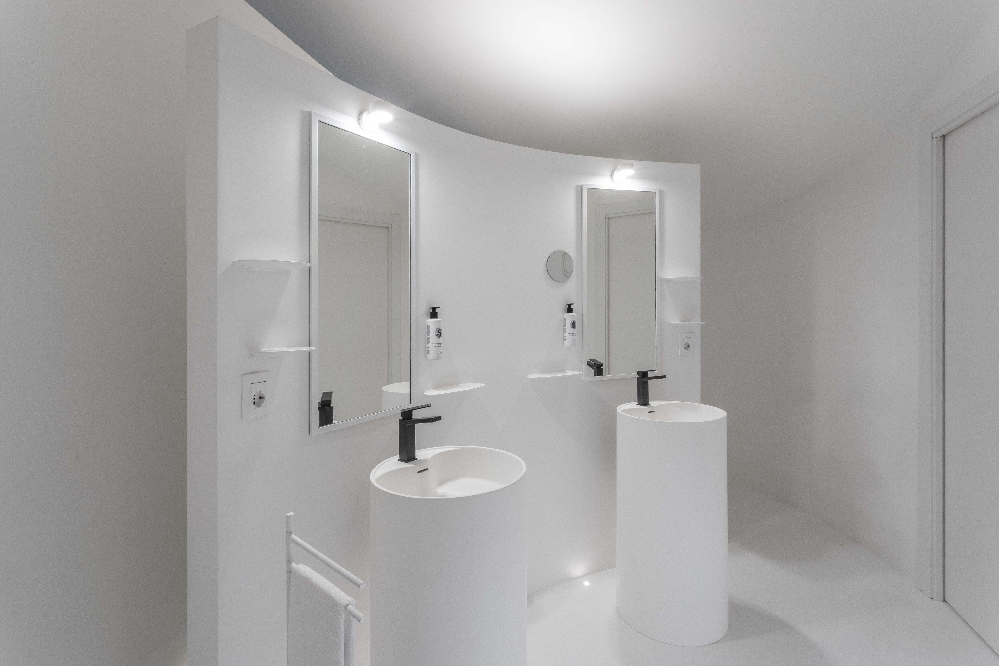 A modern bathroom with two white sinks, large mirrors, and a white vanity.