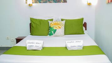 Cama arrumada com roupa de cama verde e branca, dois travesseiros e duas toalhas com a inscrição 'Stephen Hotel'.