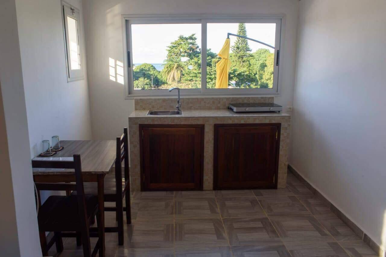 Una pequeña cocina con ventana, un lavamanos y una zona de comedor con sillas.