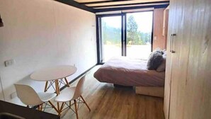 A compact room with a bed, a small table, and chairs. There is a large window providing a view of the outdoors. - Vista Mar Pupuya Matanzas Cabaña 2 (O'Higgins)